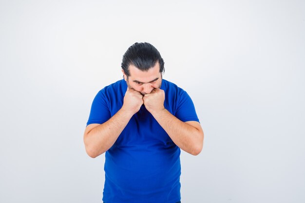 Man van middelbare leeftijd in blauw t-shirt met vuisten op mond en serieus kijkend