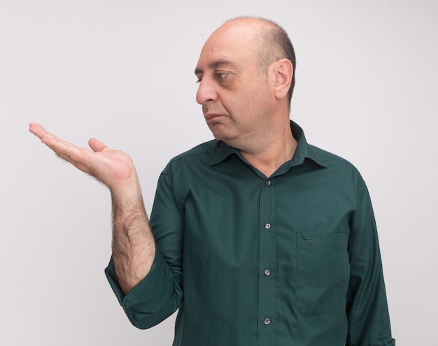 Man van middelbare leeftijd met een groene t-shirt die beweert iets in de hand te houden geïsoleerd op een witte muur met kopie ruimte