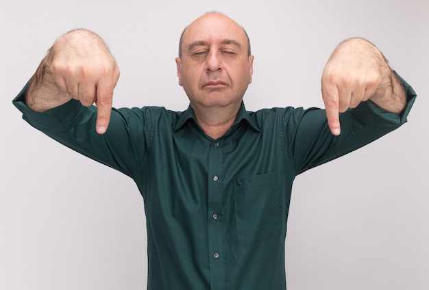 Gratis foto man van middelbare leeftijd met gesloten ogen dragen groene t-shirt wijst naar boven geïsoleerd op een witte muur