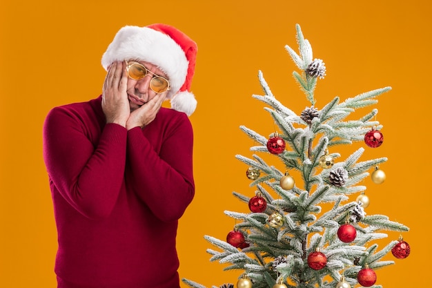 Gratis foto man van middelbare leeftijd met kerst kerstmuts in donkerrode coltrui en gele bril met droevige uitdrukking