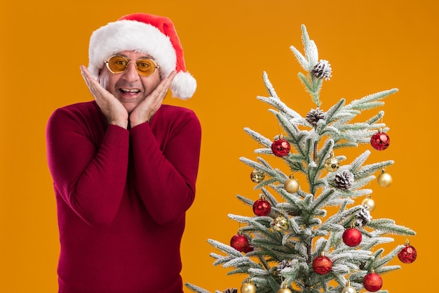 Gratis foto man van middelbare leeftijd met kerst kerstmuts in donkerrode coltrui en gele glazen blij en opgewonden