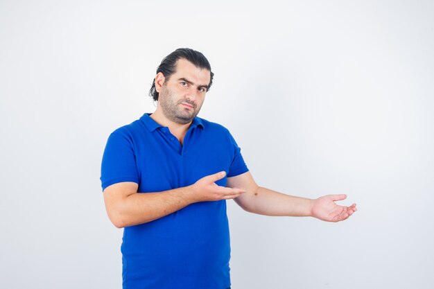 Man van middelbare leeftijd verwelkomen iets in blauw t-shirt en op zoek zelfverzekerd. vooraanzicht.