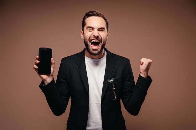 Man verheugt zich en poseert met smartphone op bruine achtergrond