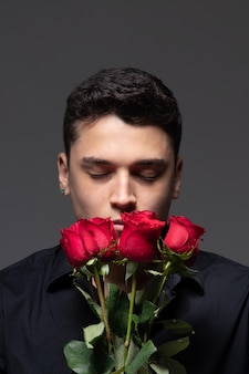 Man verliefd in donkere kleding met een boeket rode rozen foto in studio grijze achtergrond