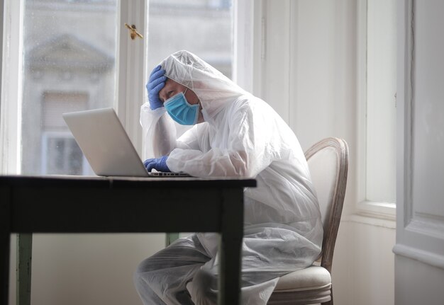 Man werkt op een computer die wordt beschermd door een medisch pak en masker