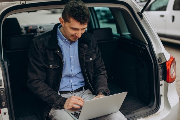 Man zit in de kofferbak van zijn auto en werkt op de computer