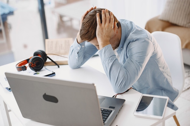 Gratis foto man zit in de woonkamer thuis. guy geniet van studeren met behulp van laptop en headset. boos.