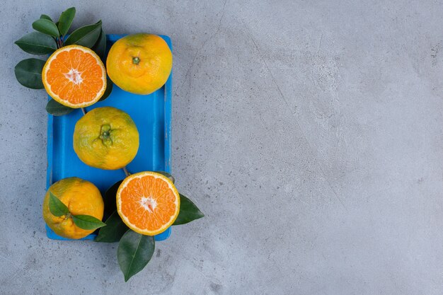Gratis foto mandarijnen en bladeren op een kleine, blauwe schotel op marmeren achtergrond.
