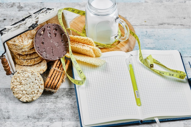 Mandje met koekjes en een potje melk op een houten tafel met een notebook.