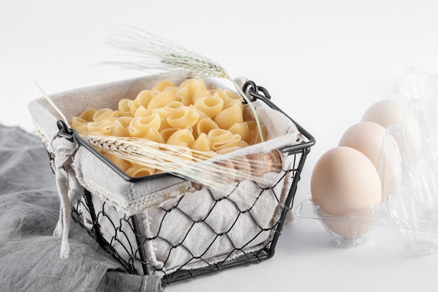 Mandje van rauwe pasta en eieren in container op wit oppervlak.