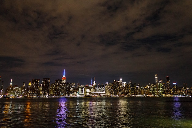 Manhattan bij nacht die van veraf met rivierbezinning is ontsproten