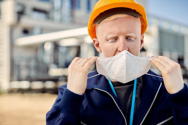 Gratis foto mannelijke albino-arbeider die een beschermend gezichtsmasker opzet terwijl hij op de bouwplaats is