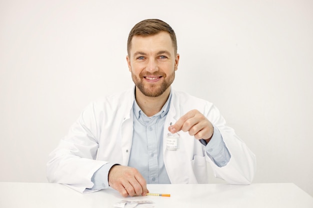 Mannelijke arts die een vaccin tegen Covid19 houdt dat op witte achtergrond wordt geïsoleerd