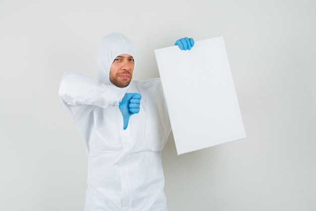 Mannelijke arts die leeg canvas houdt, die duim in beschermend kostuum toont