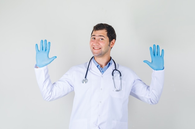 Mannelijke arts weigering gebaar beleefd in witte jas, handschoenen en op zoek vrolijk