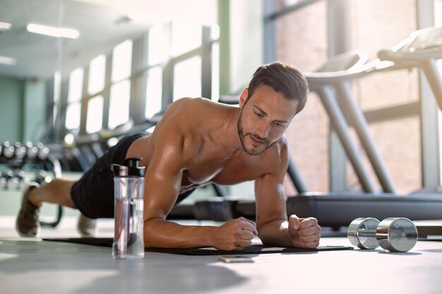 Mannelijke atleet in plank pose die kracht uitoefent tijdens sporttraining in een sportschool