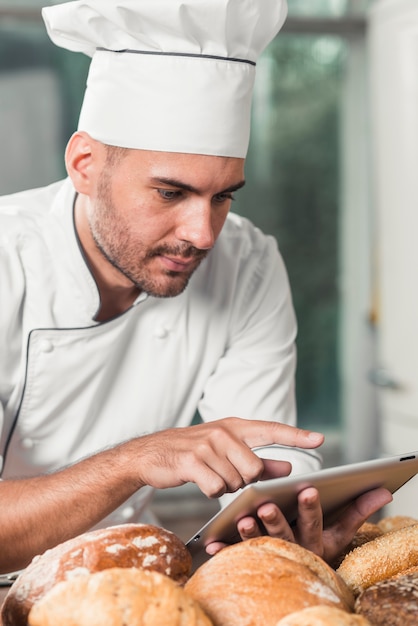 Gratis foto mannelijke bakker die digitale tablet met broden gebruikt