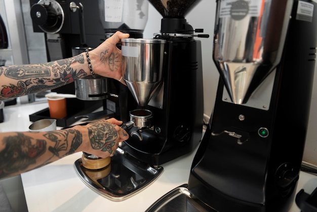 Gratis foto mannelijke barista met tatoeages met behulp van de koffiemachine in de coffeeshop