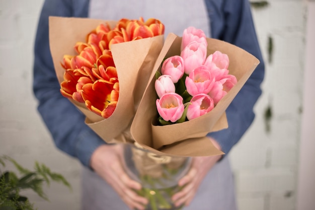 Mannelijke bloemist die roze en een oranje tulpenboeket houdt dat in document wordt verpakt