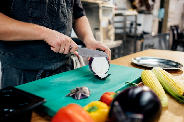 Mannelijke chef-kok aubergine snijden in de keuken