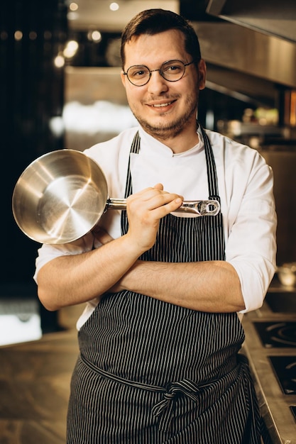 Mannelijke chef-kok bij keuken die pan houdt