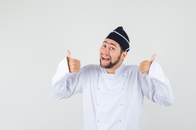 Mannelijke chef-kok die duim toont terwijl hij lacht in wit uniform en er tevreden uitziet, vooraanzicht.