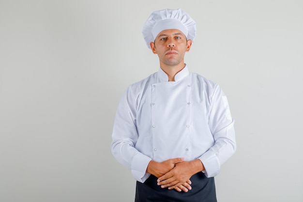 Mannelijke chef-kok die zich klaar om in uniform, schort en hoed te koken bevindt