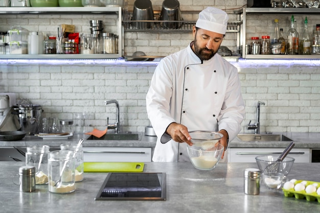 Gratis foto mannelijke chef-kok in de keuken die bloem zift