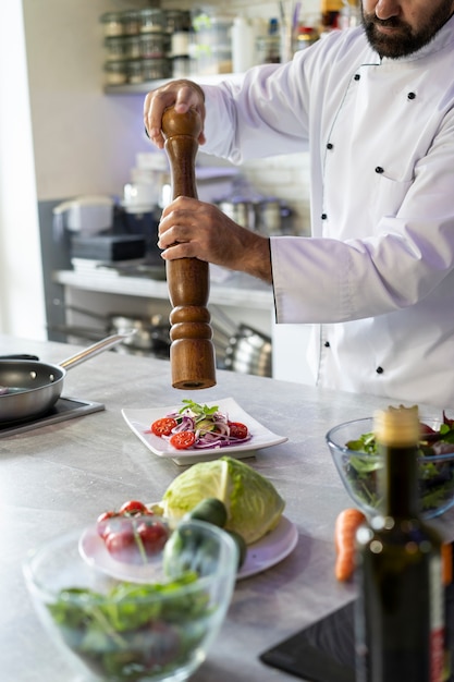 Gratis foto mannelijke chef-kok in de keuken die een bord met eten kruiden