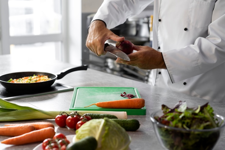 Gratis Foto mannelijke chef-kok in de keuken die groenten voor schotel hakt