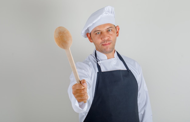 Mannelijke chef-kok in hoed, schort en uniforme tonen houten lepel