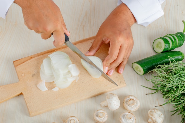 Mannelijke chef-kok in uniform hakken ui op snijplank in de keuken