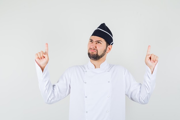 Mannelijke chef-kok in wit uniform die omhoog wijst terwijl hij fronst, vooraanzicht.