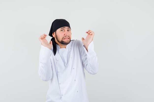 Mannelijke chef-kok in wit uniform hand in hand in overgavegebaar en ziet er bang uit, vooraanzicht.