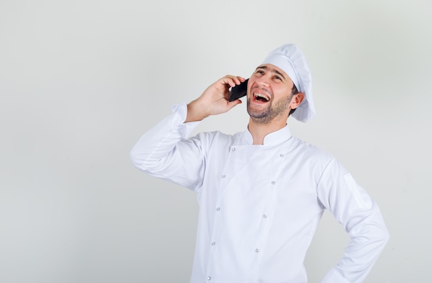 Mannelijke chef-kok lachen tijdens het gesprek aan de telefoon in wit uniform