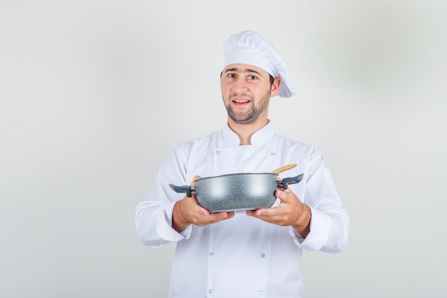 Mannelijke chef-kok soep in steelpan in wit uniform houden en gelukkig kijken