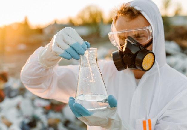 Gratis foto mannelijke ecoloog in stralingspak, gasmasker. reageerbuis met vloeistof vasthouden tijdens het bestuderen van vuilnisbelt.