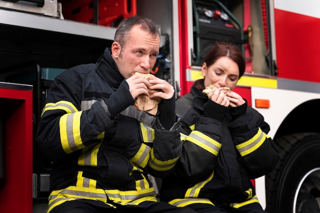 Gratis foto mannelijke en vrouwelijke brandweerlieden op het station samen aan het lunchen