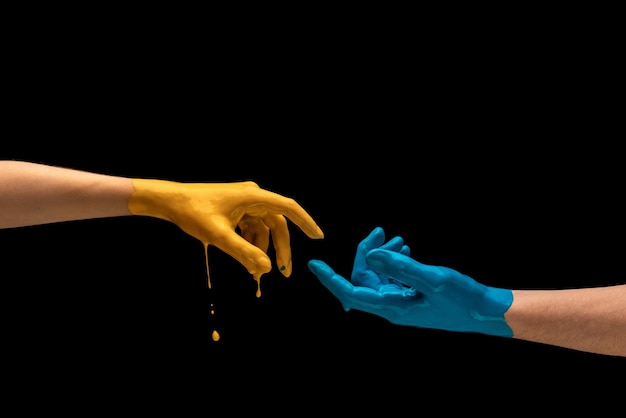 Mannelijke en vrouwelijke handen in gele en blauwe verf proberen elkaar te bereiken geïsoleerd op zwarte achtergrond