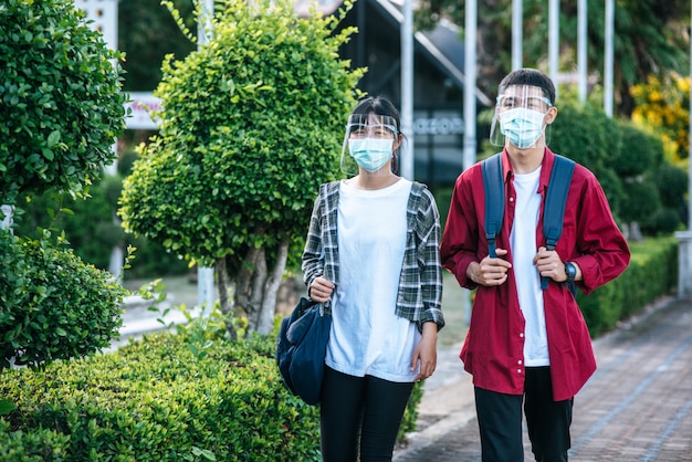 Mannelijke en vrouwelijke studenten dragen een chill gezicht en maskers. Loop over het voetpad