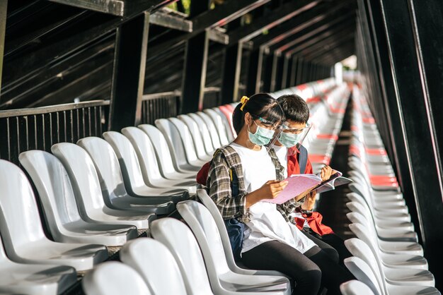 Mannelijke en vrouwelijke studenten dragen maskers en zitten en lezen op de veldstoel