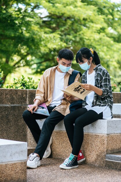 Mannelijke en vrouwelijke studenten met maskers zitten en lezen boeken op de trap