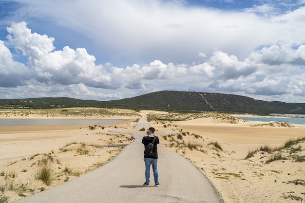 Gratis foto mannelijke fotograaf die overdag door een strand onder een bewolkte hemel in andalusië, spanje loopt