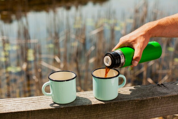 Mannelijke gietende drank in koppen bij rivier