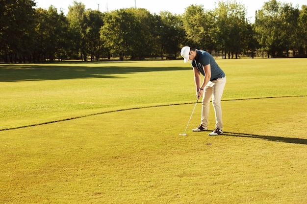 Mannelijke golfspeler die golfbal op groen zet