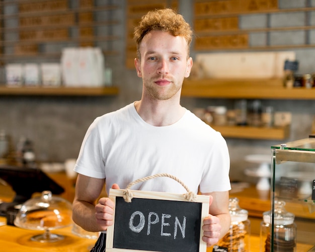 Mannelijke kelner die open teken voor koffiewinkel houdt