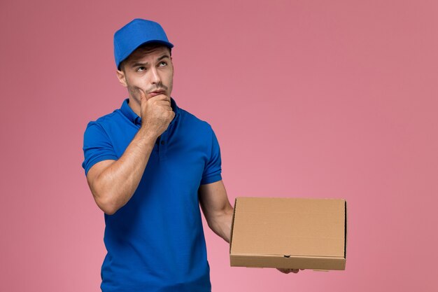 mannelijke koerier in blauw uniform bedrijf bezorgdoos met voedsel denken op roze, baan werknemer uniforme dienstverlening