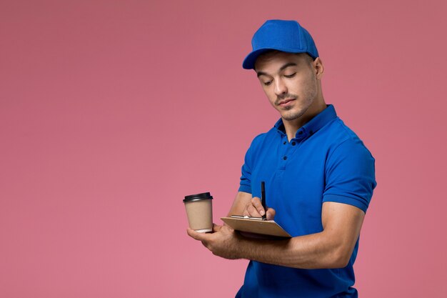 mannelijke koerier in blauw uniform koffiekopje vast te houden en notities op te schrijven over roze, werknemer uniforme dienstverlening