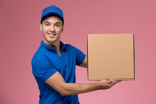 mannelijke koerier in blauw uniform met bezorgdoos met voedsel op roze, arbeiders uniforme dienstverlening