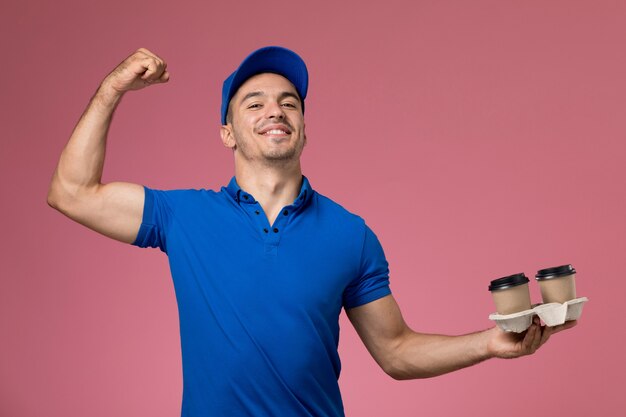 mannelijke koerier in blauw uniform met koffie en buigen op roze, werknemer uniforme dienstverlening